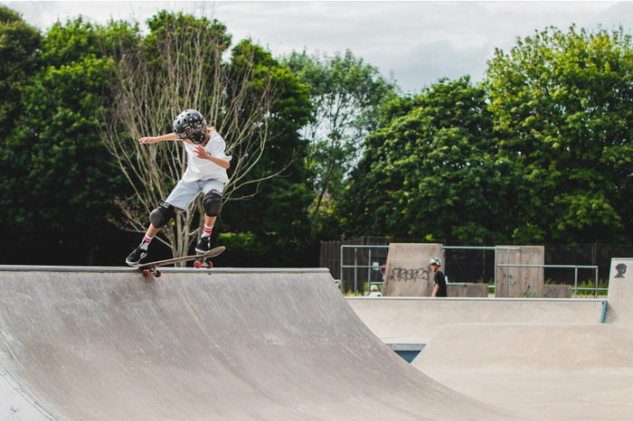 Image of a young person on a skateboard balancing at the top of a ramp, wearing a helmet and knee pads