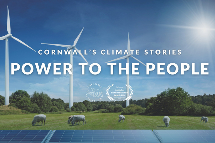 Wind turbines in a field on a sunny day with solar panels. Text that reads 'Cornwall's climate stories, power to the people'
