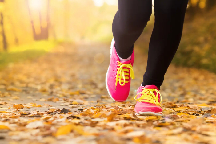 Close up of the bottom of someone's legs wearing trainers walking on a path covered in autumn leaves