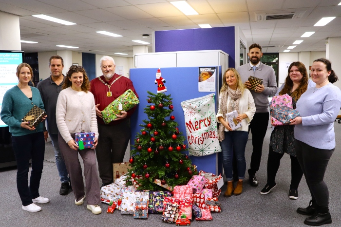 The Chairman of the council, Cllr Stephen King, holding a present next to a Christmas tree with presents underneath. Surrounding him are council staff also holding gifts.