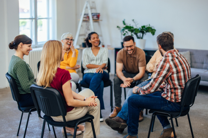 Group of adults sat on chairs in a circle, talking and smiling