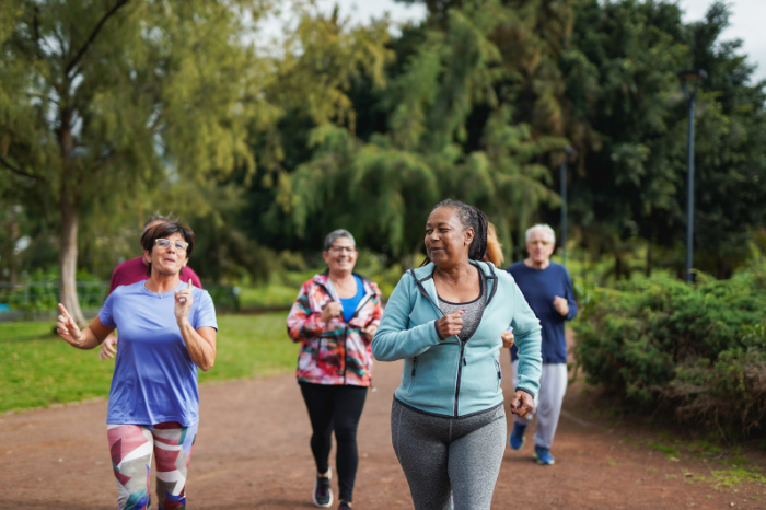 Group of people smiling whilst running together on a path with trees and grass to the side