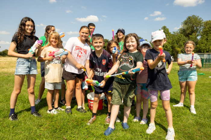 Group of children outdoors on a sunny day, holding water pistols and smiling