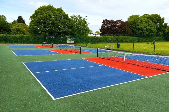 Three pickleball courts with nets and a blue ground. Trees in the background