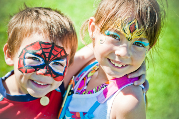 Two children smiling outside with their faces painted.