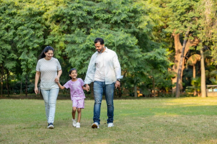 Family of people, a woman, a man and a girl, walking hand in hand across a field surrounded by trees