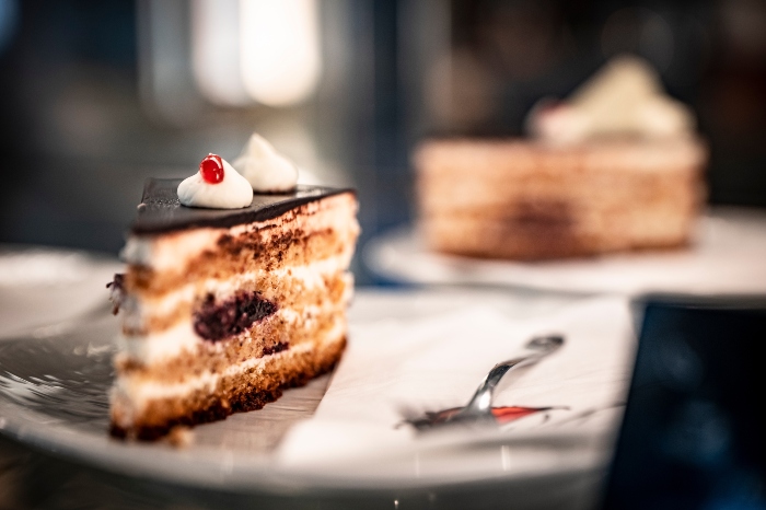 A slice of chocolate cake on a plate with a fork with the whole cake in the background