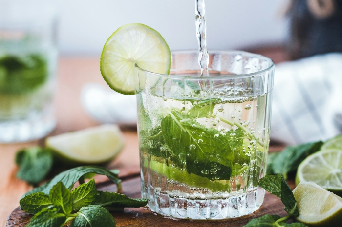 Gin being poured into a glass with mint and a slice of lime