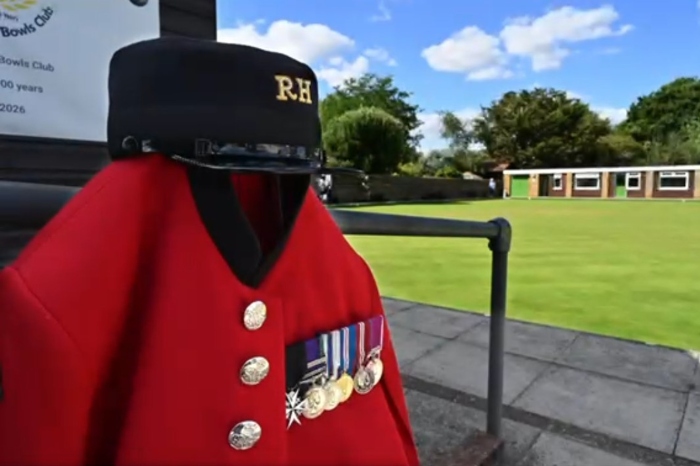 Red uniform with medials. Bowling green in background with some outhouses