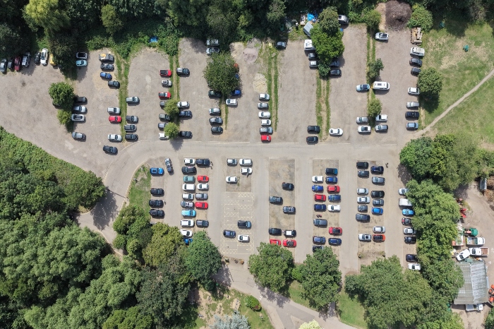 Bird's eye view of a nature reserve's car park. Some cars are parked and has a small open to the right, behind the depot.