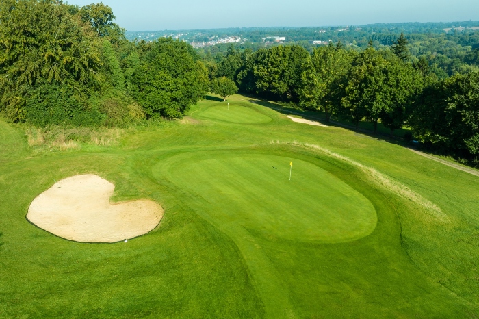 A bird's eye view of a green golf course with a sand pit and golf flag near the hole