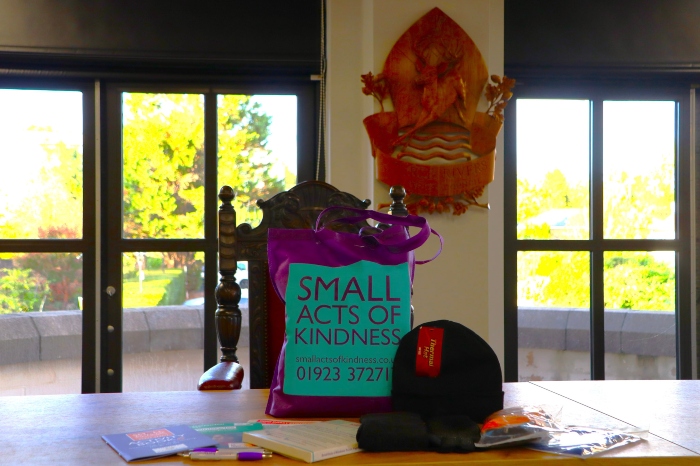 Small Acts of Kindess tote bag in council chamber with wooly hat, gloves, pens, notepad and leaflets